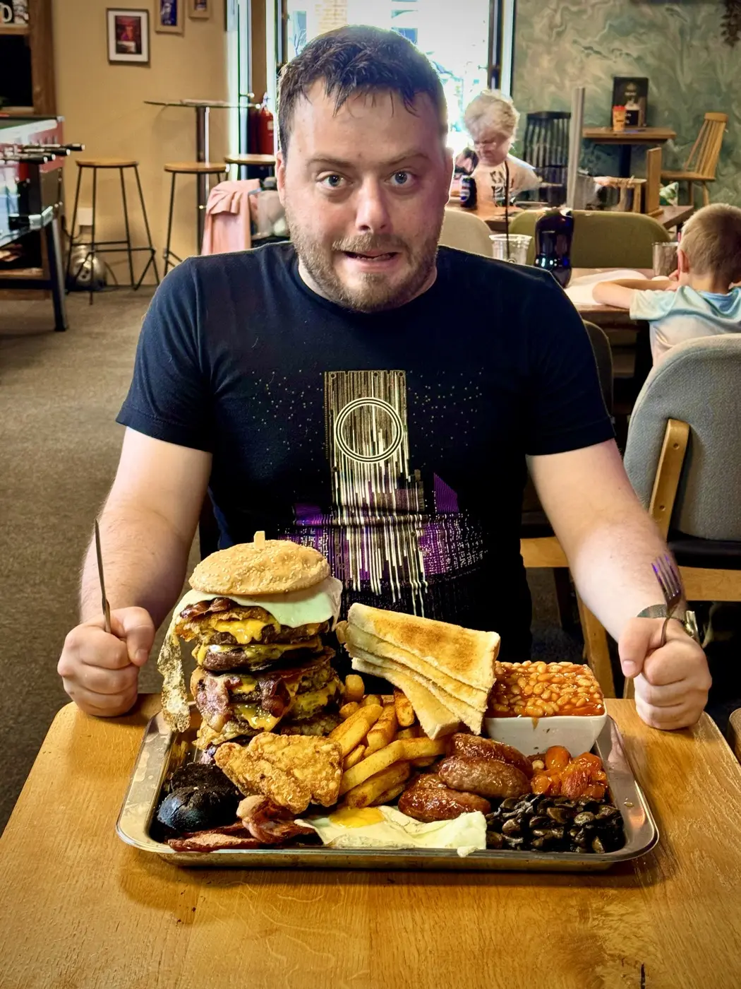 The Brunch Challenge Burger at Revive Cafe Norwich - a six-patty burger tower with a full English breakfast and seasoned fries on one tray, with a challenger ready to attempt it